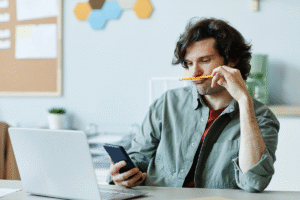 Man sits at desk, scrolling on phone as he searches articles about untreated ADHD